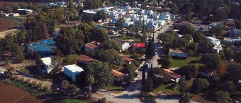 An aerial view of a residential area with houses, a tennis court, and surrounding greenery.