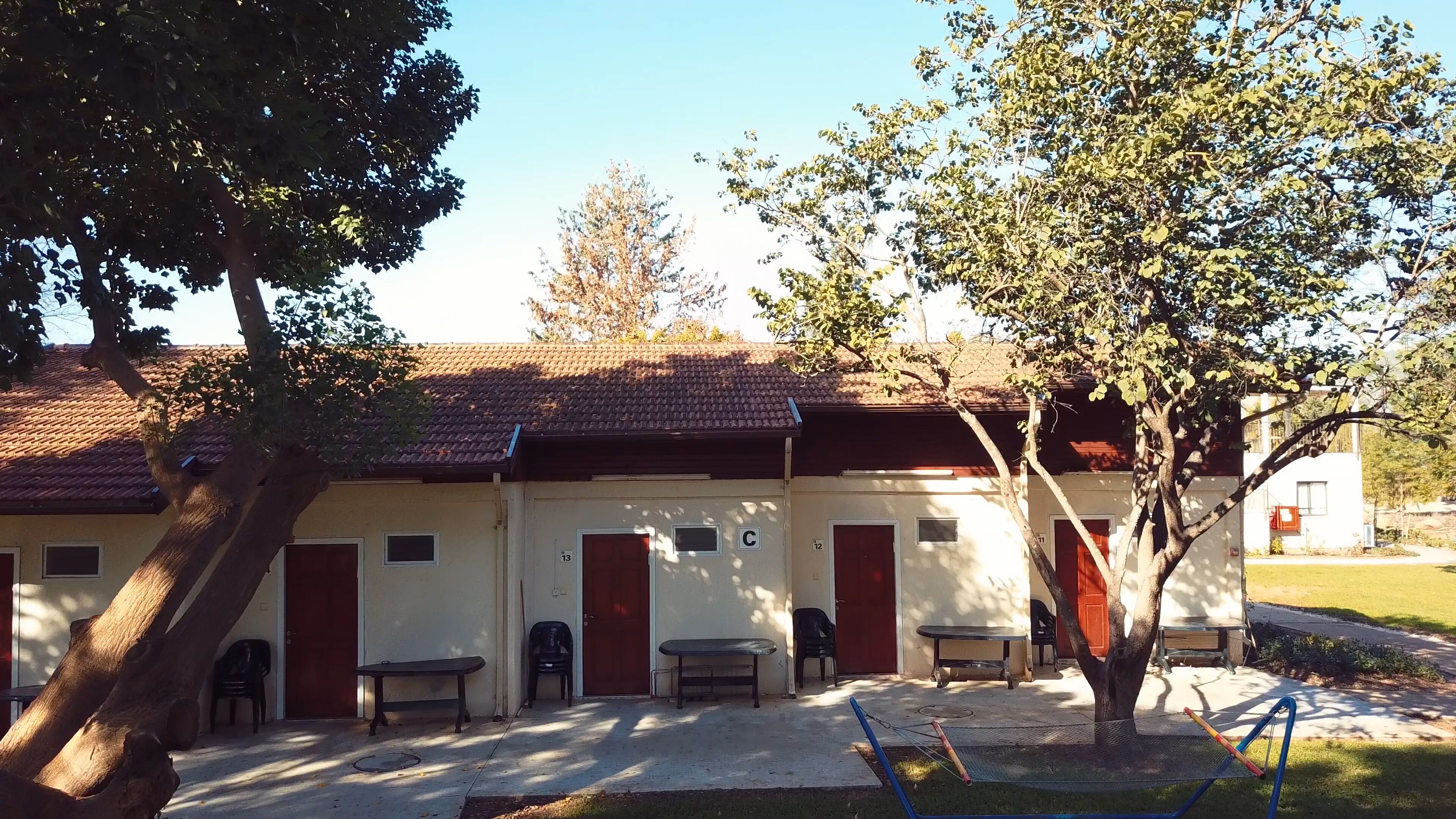 Un bâtiment doté d’un toit en tuiles, de chambres numérotées et d’un espace extérieur aménagé pour s’asseoir.