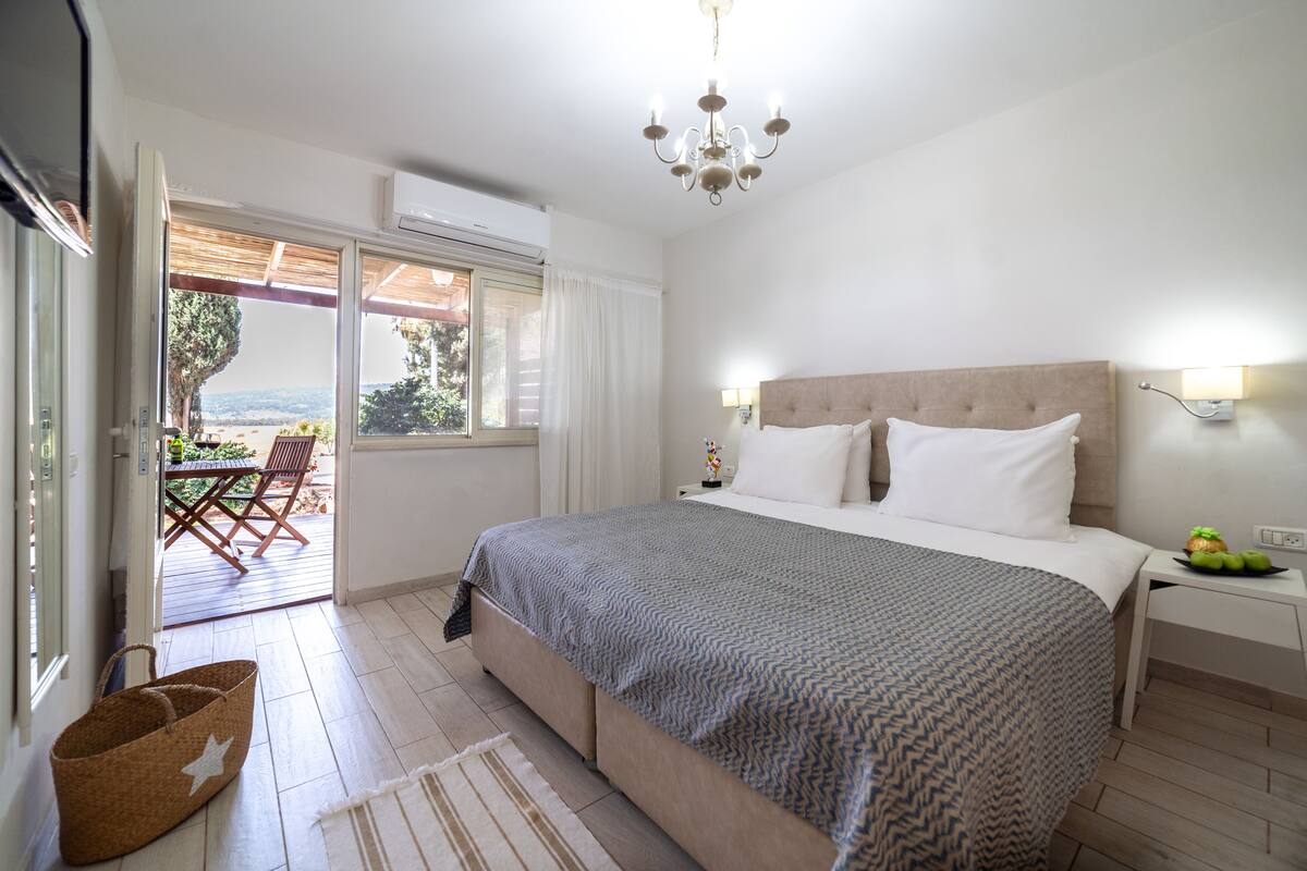 Ein Schlafzimmer mit einem großen Bett, einer Chandelier, einem Nachttisch und Blick ins Freie.