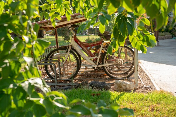 A bicycle parked on a metal rack in a garden area with grass and trees.