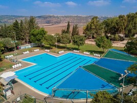 Piscina com várias pistas, rodeada por árvores e vista para colinas ao longe.