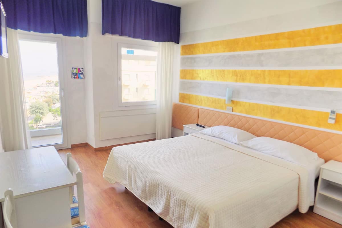 A bedroom with a bed, bedside tables, a desk, and a window with curtains.