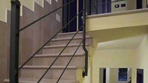 A staircase with beige steps and a metal handrail, leading to a landing with a door and a window. - Il Pagliericcio (Ferrara)