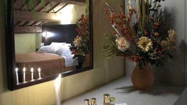 A bathroom with a mirror, a vase of flowers, a candle, and toiletries on the counter. - Il Pagliericcio (Ferrara)