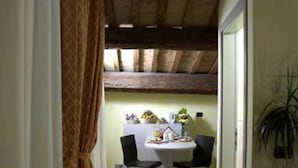 A narrow hallway leading to a dining area with a table and chairs, a ceiling with exposed beams, and a potted plant. - Il Pagliericcio (Ferrara)