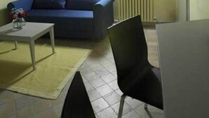 A room with a blue sofa, a small table with a vase, a chair, and a radiator. - Il Pagliericcio (Ferrara)