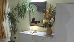 A room with a white cabinet, a potted plant, a vase with flowers, and a suitcase on the floor. - Il Pagliericcio (Ferrara)