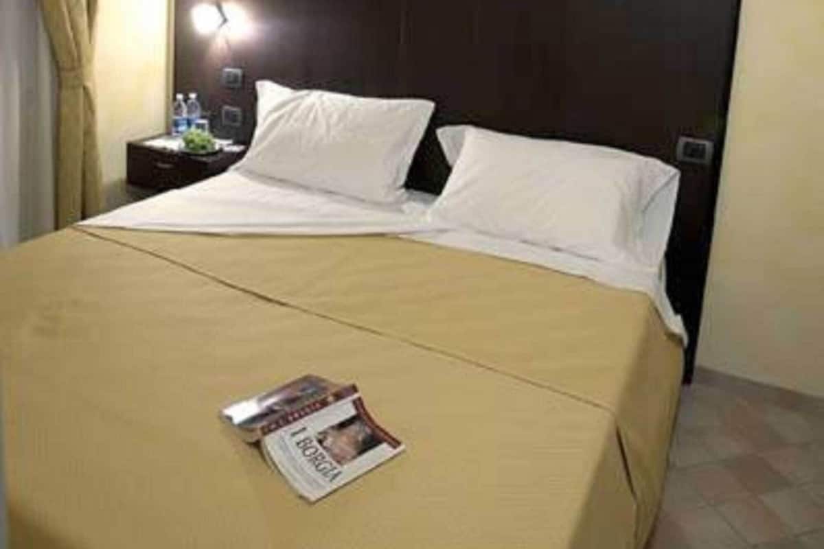A hotel room with a bed, a nightstand, a lamp, and a magazine on the bed.