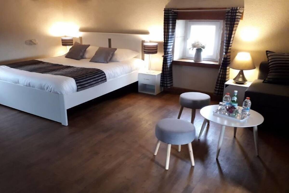 A bedroom with a bed, bedside tables, a small round table with bottles, and a window with curtains.