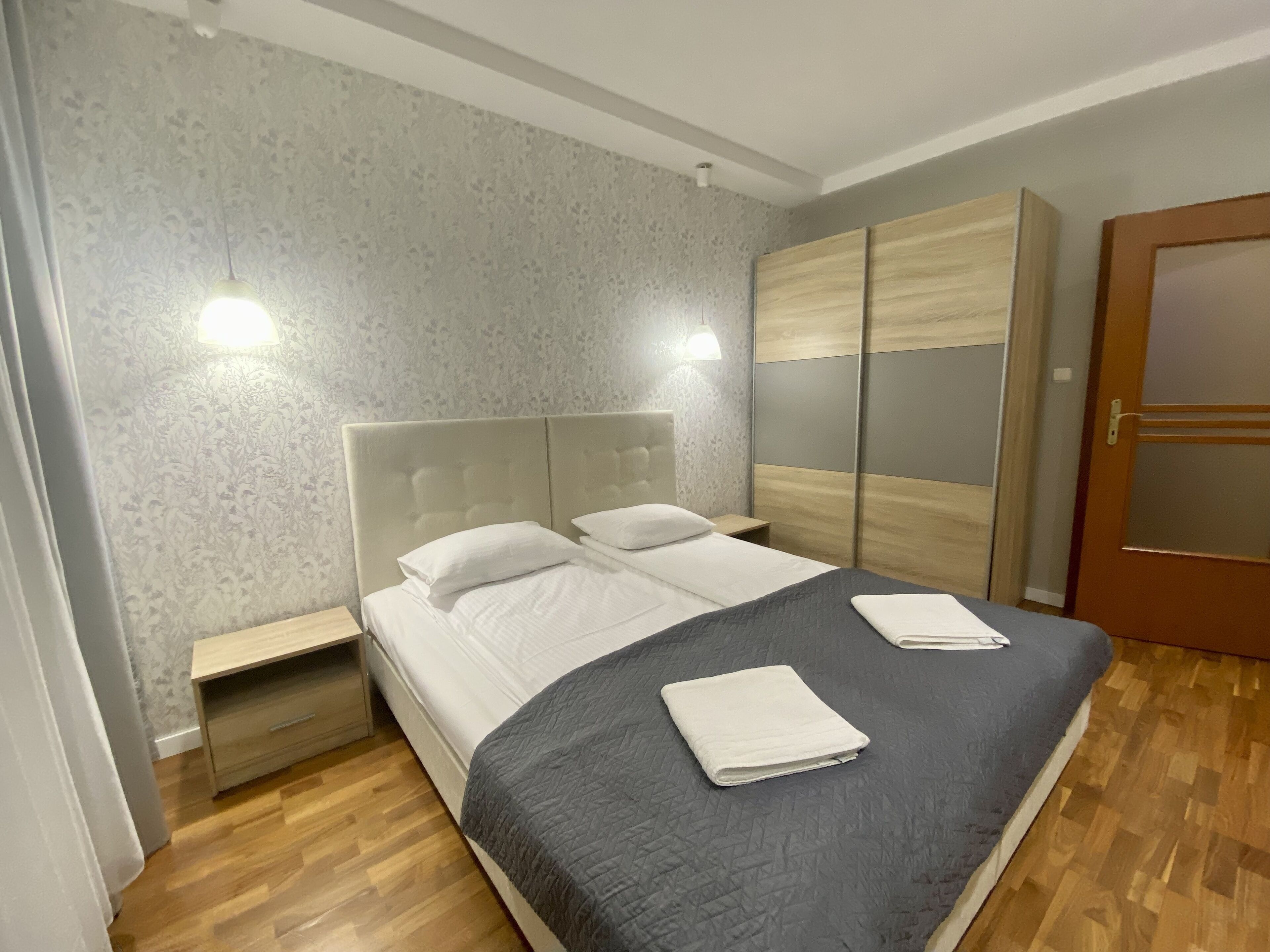 Ein ordentlich eingerichtetes Schlafzimmer mit einem Bett, zwei Nachttischen, einem Kleiderschrank und einer Tür.