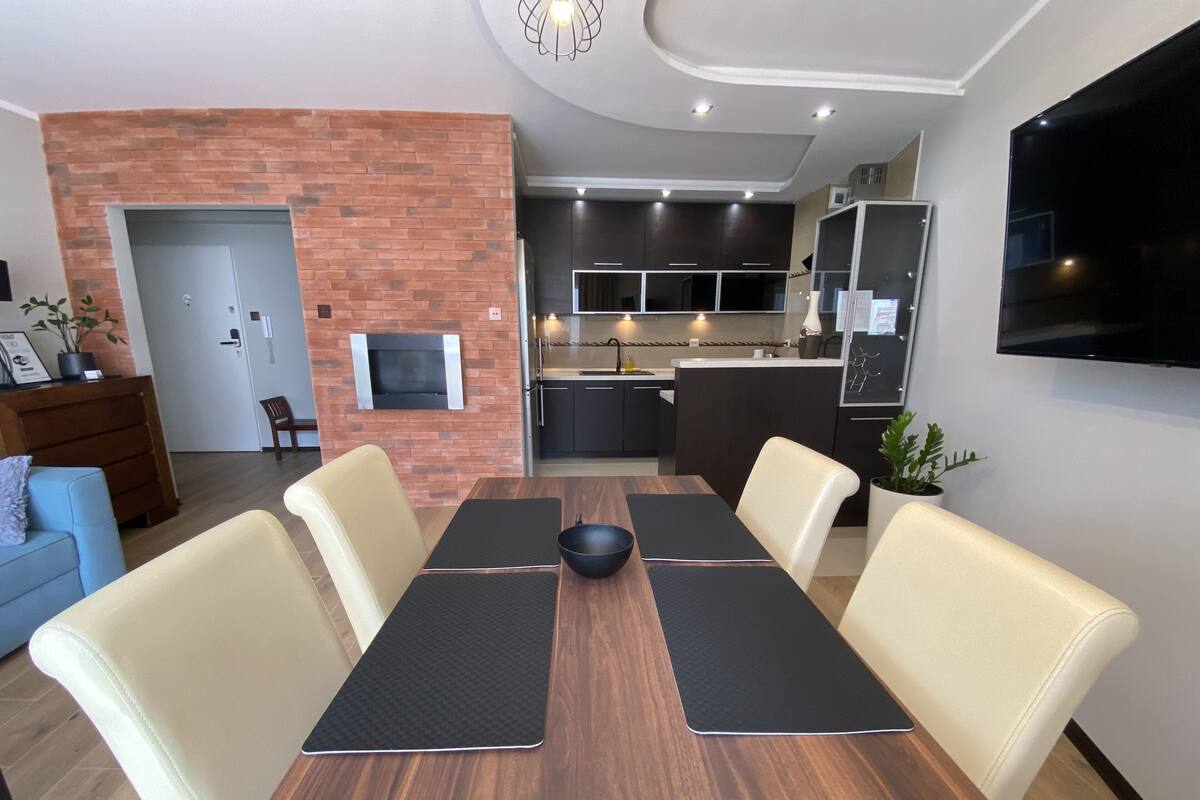 A modern dining area with a wooden table, cushioned chairs, and a black bowl in the center.