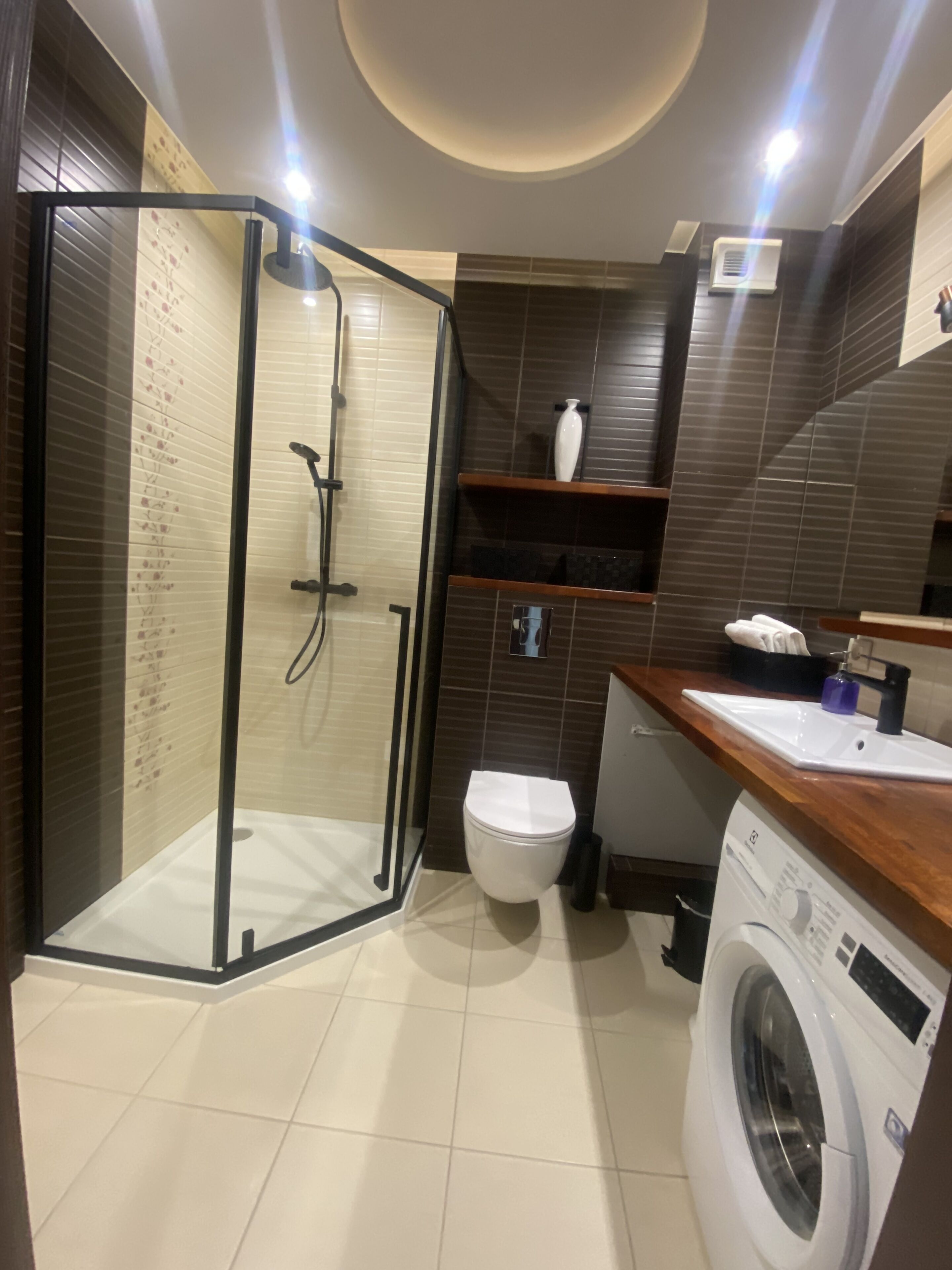 A modern bathroom with a glass-enclosed shower, a toilet, a washing machine, and a sink.