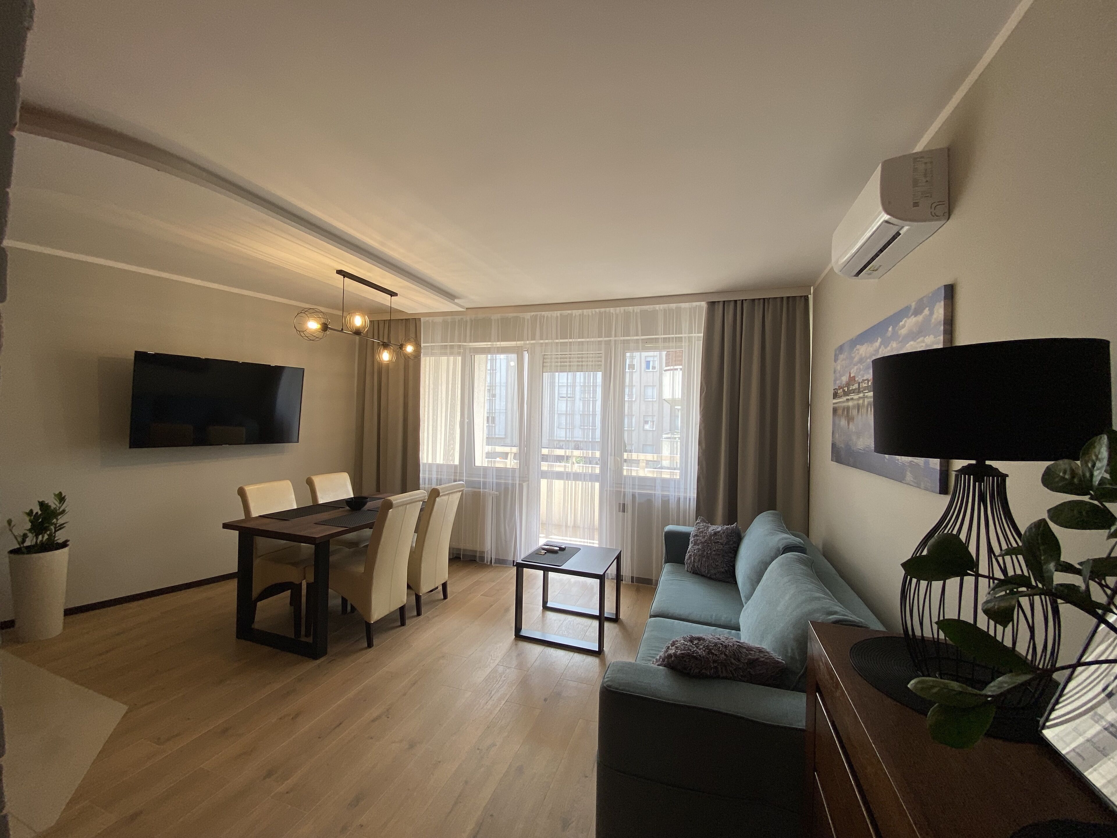 Een moderne woonkamer met een eethoek, een bank, een televisie en een plant.