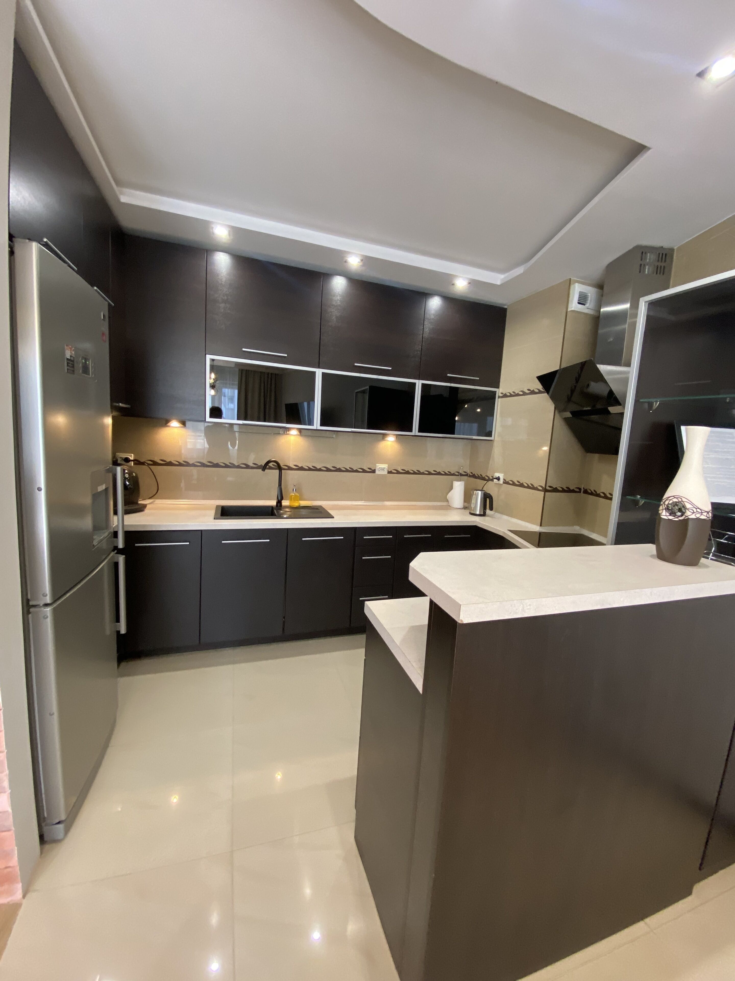 Una cocina moderna con armarios oscuros, un refrigerador de acero inoxidable, un lavamanos y una encimera.
