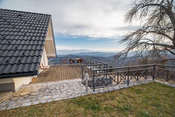 Eine Terrasse mit einem gepflasterten Weg, der zu einem Holzboden führt, mit Blick auf eine Berglandschaft.
