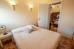 Ein Schlafzimmer mit Bett, Nachttisch, Lampe und einer Tür zu einem anderen Raum.