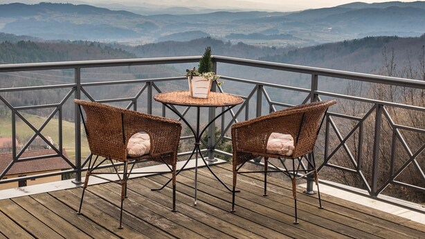 Un balcón con sillones de mimbre y una mesita pequeña, con vistas a un paisaje montañoso.