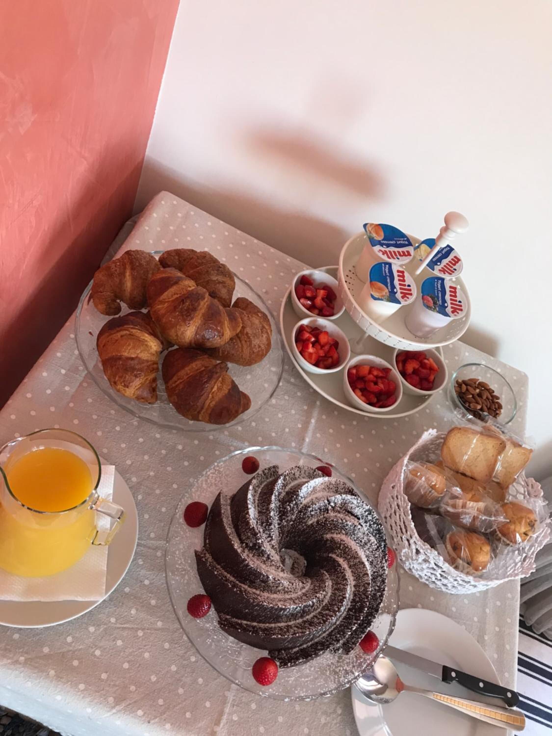 Una mesa de desayuno con cruasanes, un pastel de chocolate y una jarra de jugo de naranja.