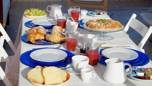 Een ontbijttafel met croissants, brood, sap en een schaal fruit.