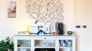 Een witte kast met glazen deuren, een decoratief metalen blad aan de muur, een kleine potplant en een witte emmer.