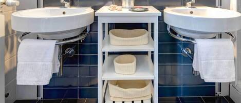 A bathroom with two white sinks, a white vanity, and three beige baskets on shelves.