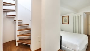 Quarto com cama, parede branca, quadro emoldurado e radiador.