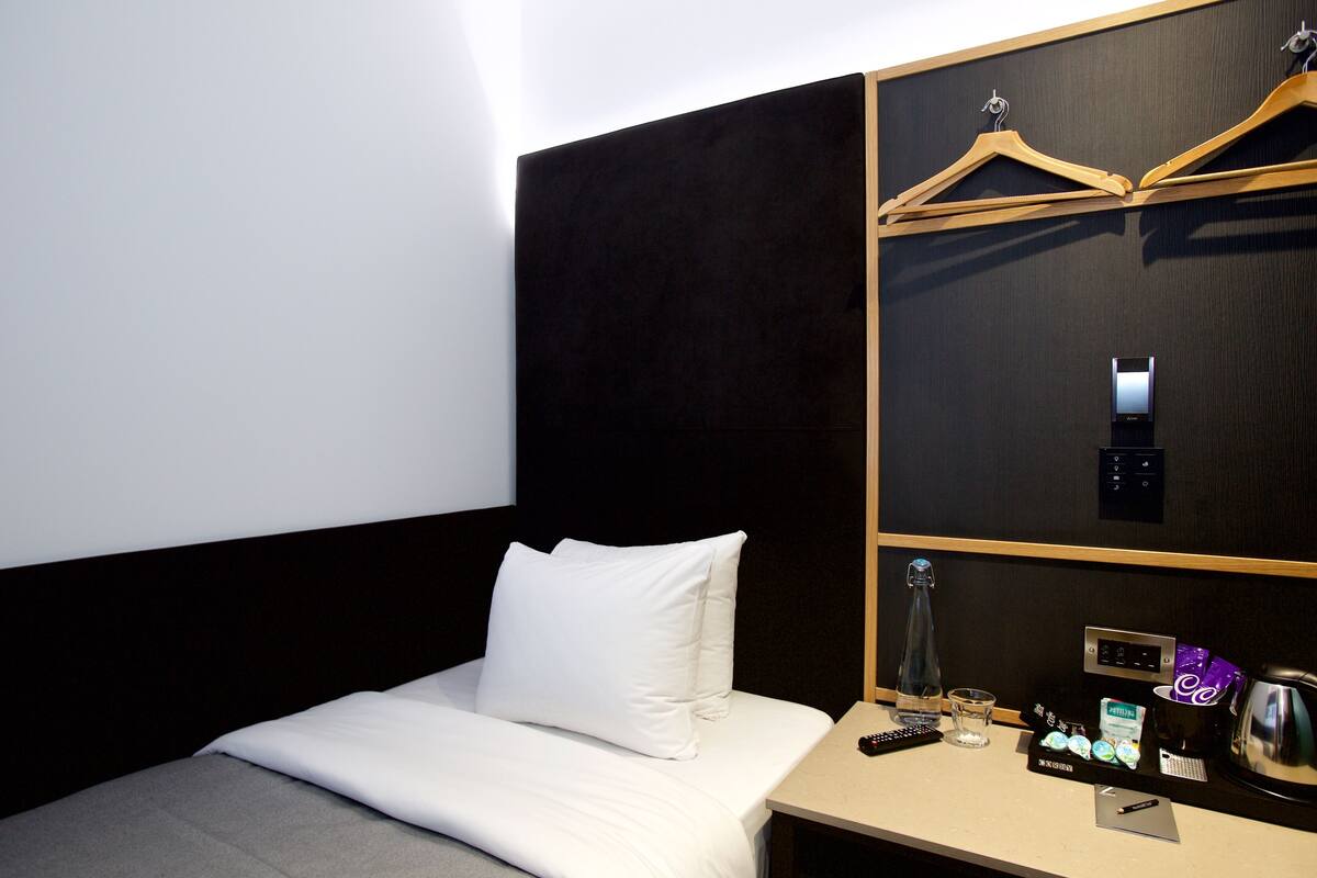 A hotel room with a bed, a bedside table, a minibar, and a coat rack.