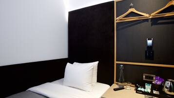 Una habitación de hotel con cama, mesita de noche, minibar y perchero.