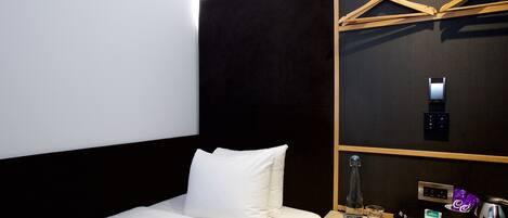 A hotel room with a bed, a bedside table, a minibar, and a coat rack.
