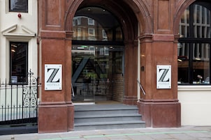 A hotel entrance with a glass door, two large pillars, and a staircase leading inside.