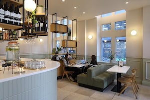 A modern bar area with wine bottles, glasses, and a counter. There are seating areas with tables and chairs.