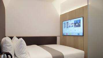 Quarto de hotel com cama, almofadas, controle remoto, caneca e televisão exibindo um canal de hotel.
