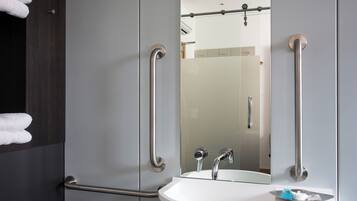 A modern bathroom with a white sink, a large mirror, and two grab bars.