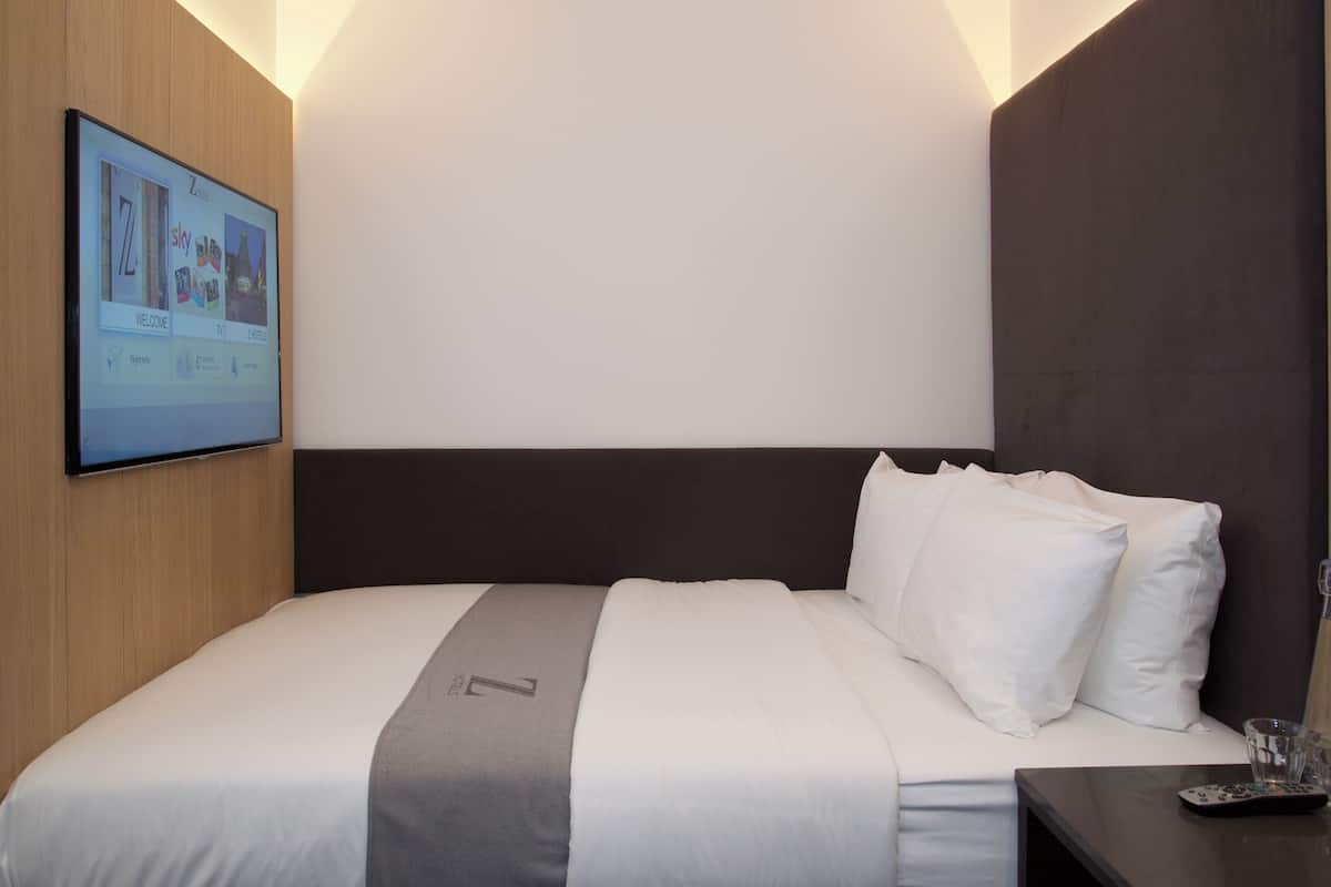 A hotel room with a bed, a TV screen displaying a welcome screen, and a remote control on a nightstand.