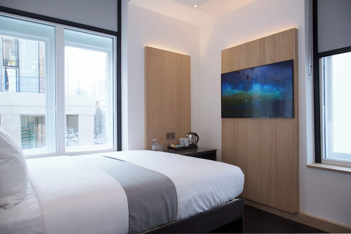 A modern hotel room with a large bed, a wooden panel wall, a painting, and a window with a city view.
