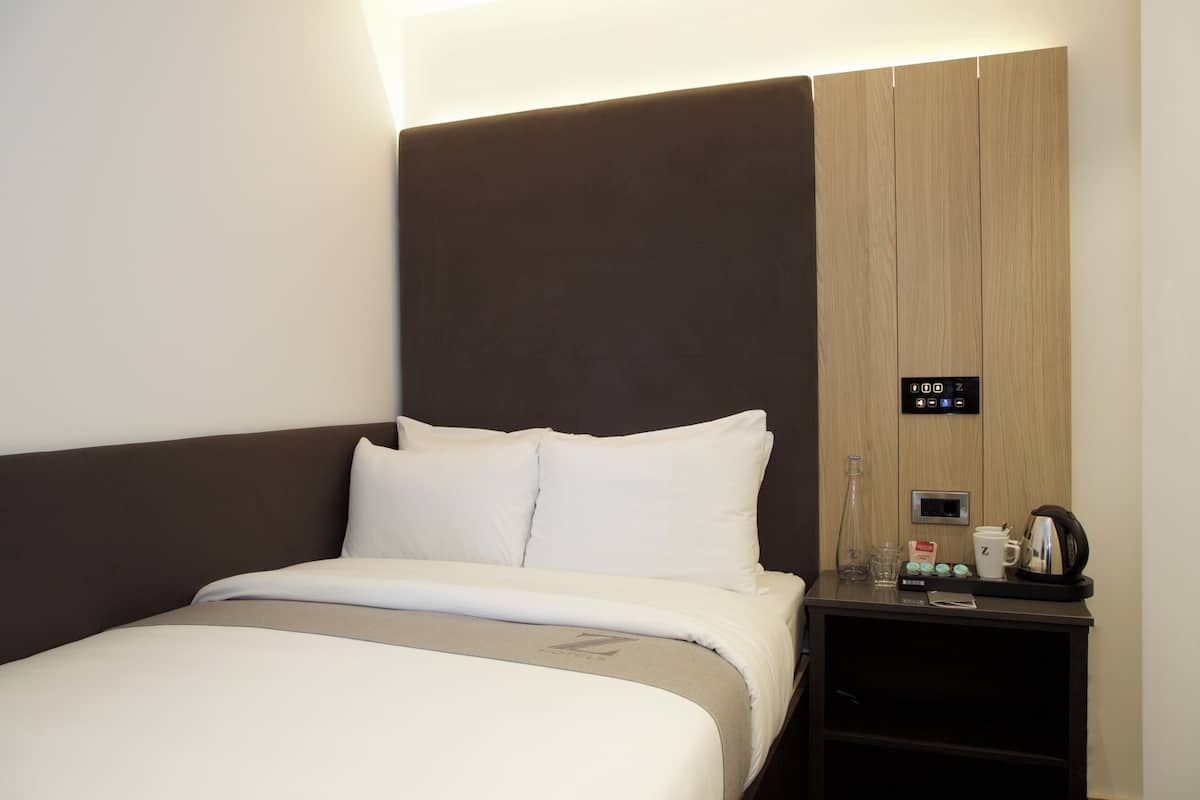 A hotel room with a bed, a nightstand, and a control panel on the wall.