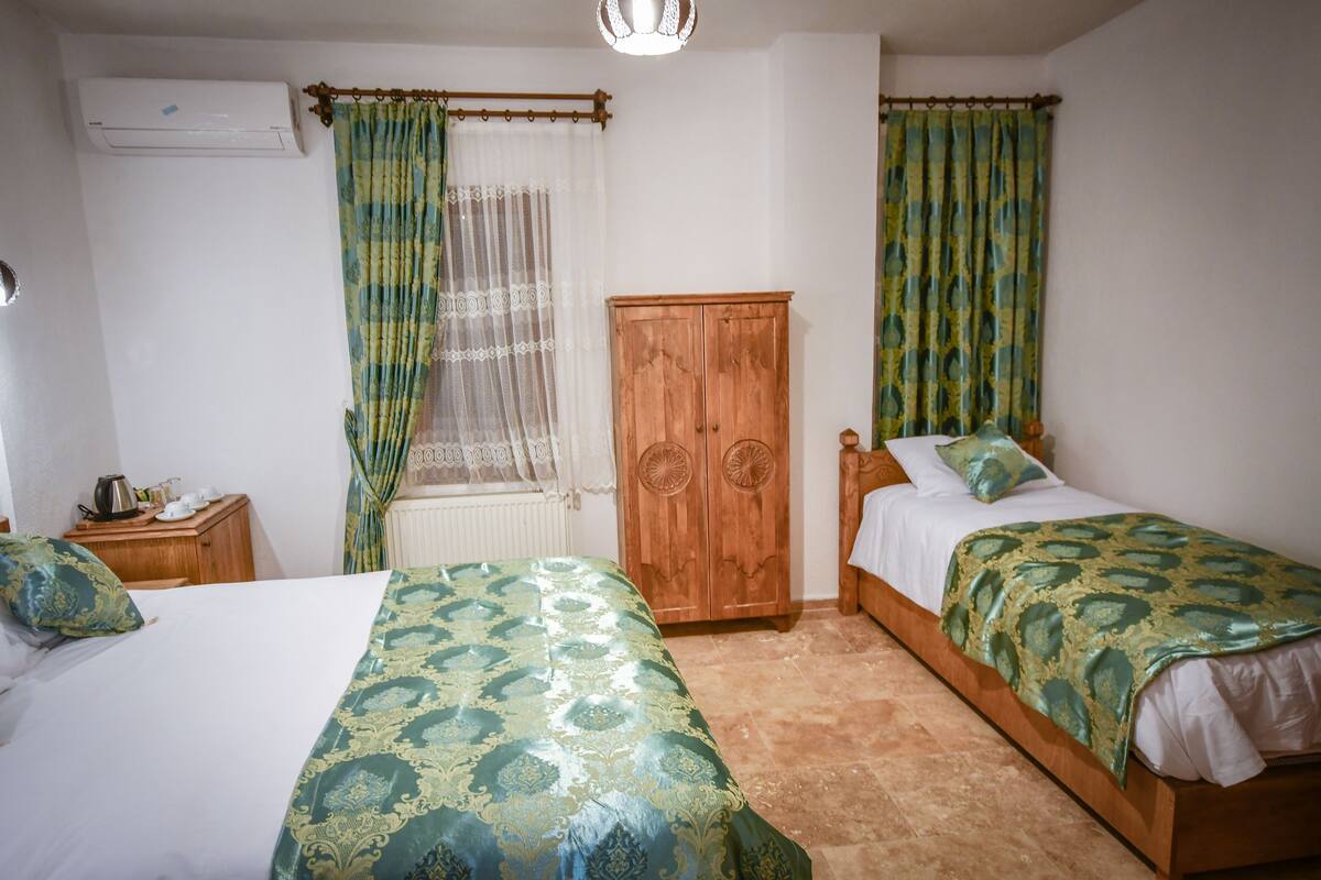 A bedroom with two beds, a wooden wardrobe, a radiator, and a window with curtains.