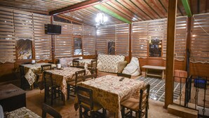 Ein Restaurant mit Holzwänden, Tischen mit gemusterten Tischdecken und einem an der Wand befestigten Fernseher.