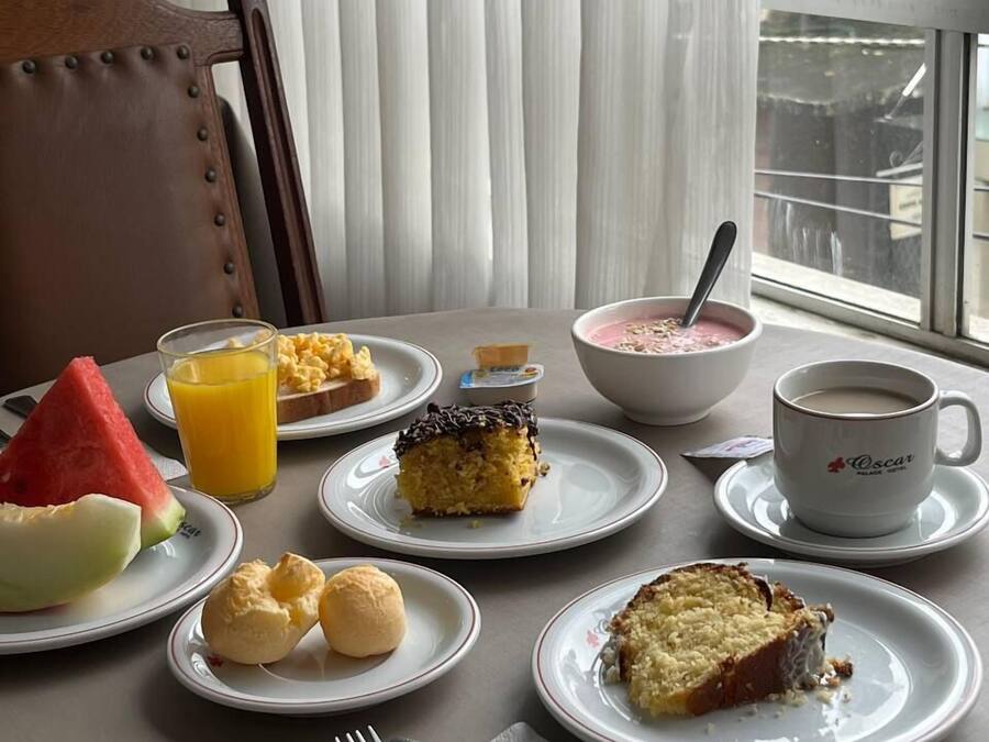 A breakfast table with plates of food, a bowl of cereal, a glass of orange juice, a cup of coffee, and a fork and knife set.