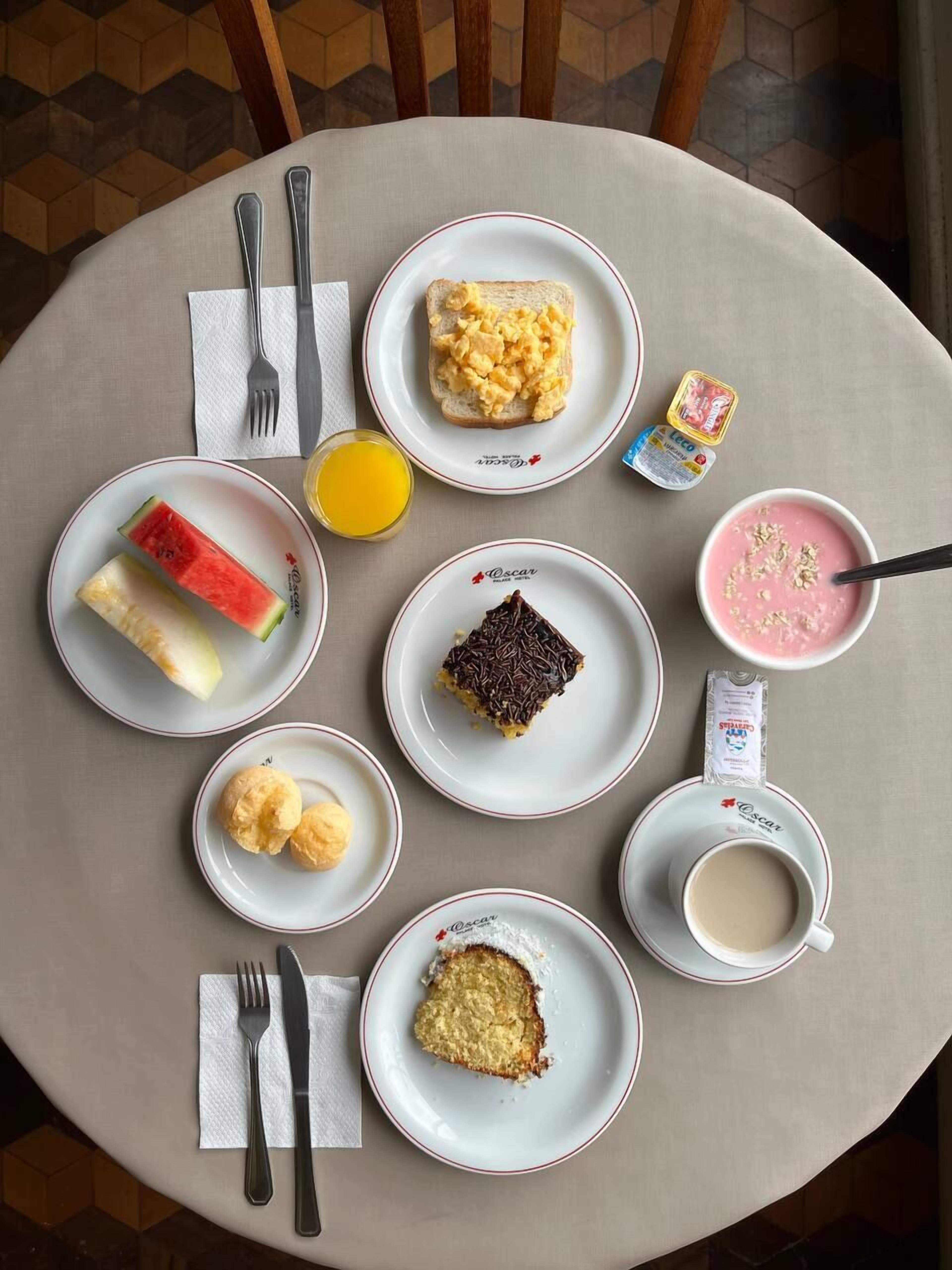 Une table ronde sur laquelle sont disposés des aliments pour le petit-déjeuner, notamment des toasts, des œufs brouillés, une part de gâteau, un bol de soupe, un verre de jus d’orange et une tasse de café.