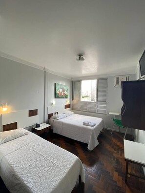 A hotel room with two beds, a desk, a chair, a TV, and a window with blinds. - Oscar Palace Hotel (Tubarao)