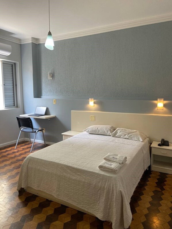 A hotel room with a bed, a desk with a laptop, a chair, and two wall-mounted lights. - Oscar Palace Hotel (Tubarao)