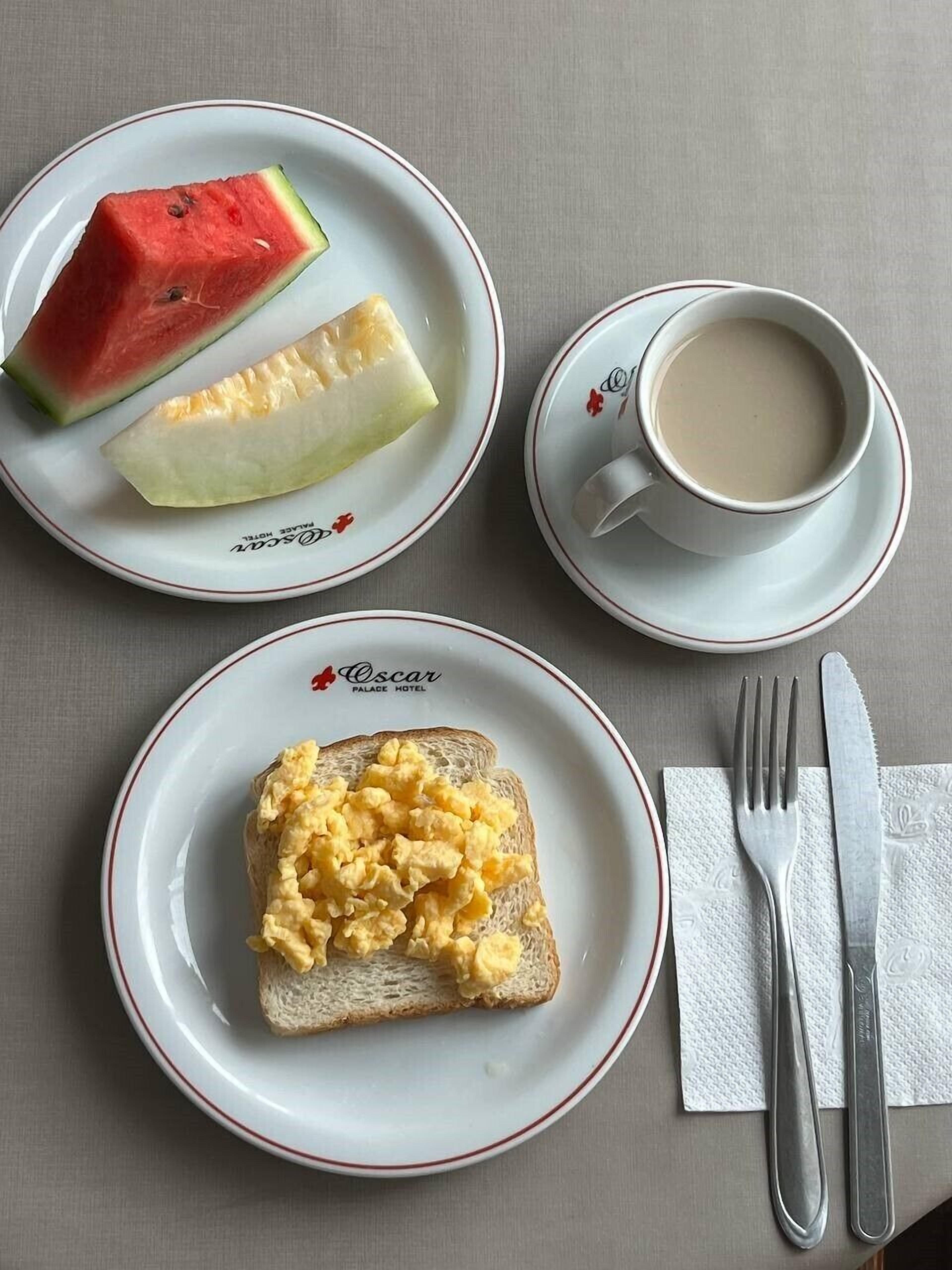 A breakfast setting with toast, scrambled eggs, a slice of watermelon, and a cup of coffee on a table.