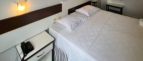 A hotel room with a large bed, bedside tables, a desk with a phone, and a painting on the wall.