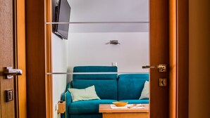 A room with a wooden floor, a teal sofa with cushions, a small wooden table, and a mounted television. - Apartments BBI (Luce)