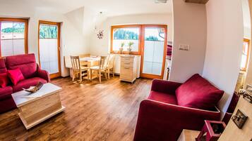 A cozy living room with a red sofa, wooden coffee table, and a dining area with a table and chairs.