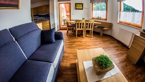 A modern living room with a sofa, dining table, chairs, and a view of the outdoors. - Apartments BBI (Luce)