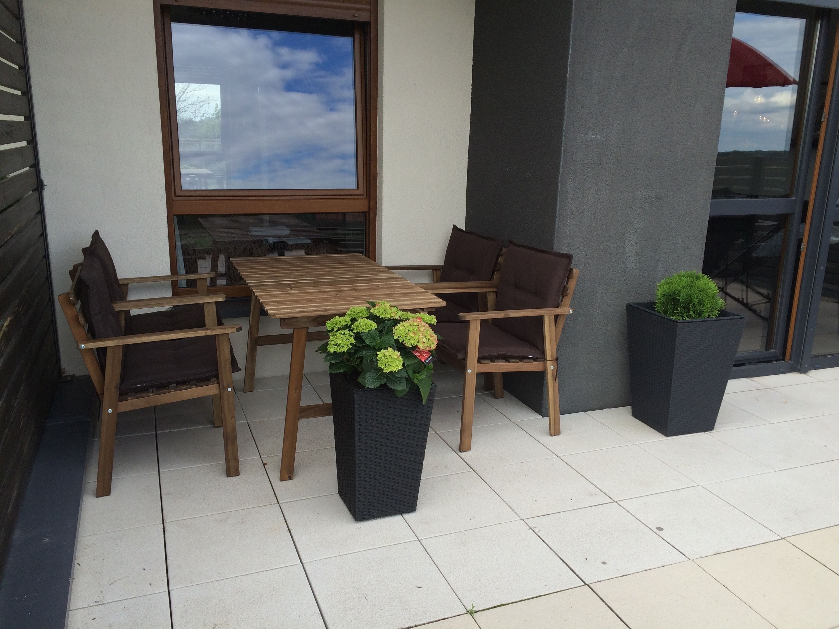 Un patio al aire libre con una mesa y sillas de madera, una planta en maceta y vista al cielo a través de una ventana.