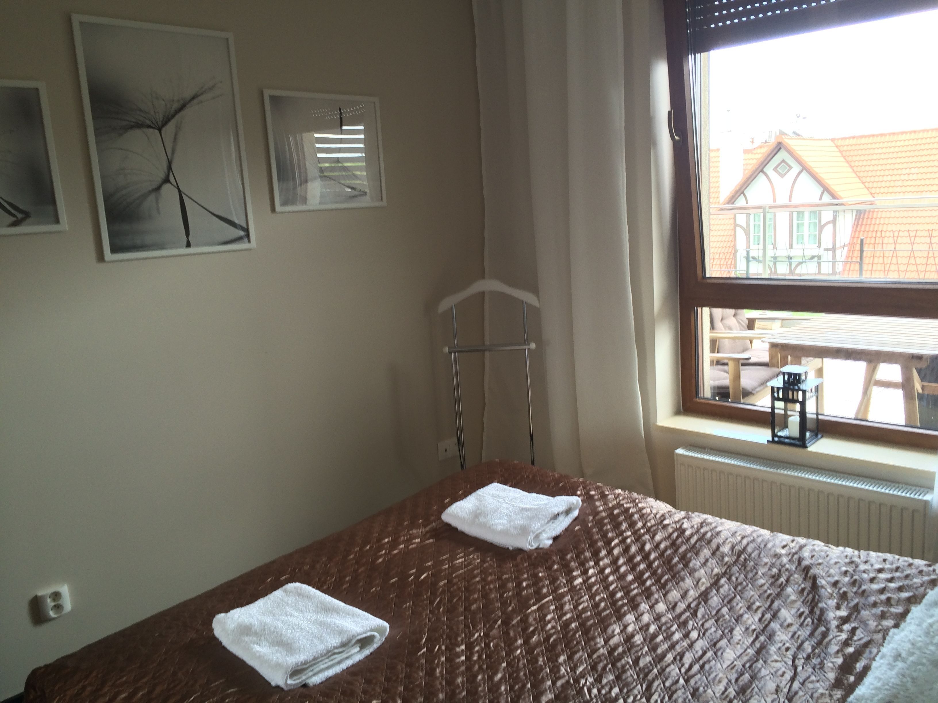Ein Schlafzimmer mit einem Bett, zwei Handtüchern, einem Heizkörper, einem Fenster mit Blick auf ein Gebäude und zwei Wandbildern.