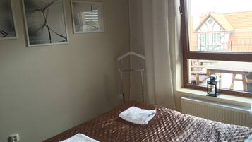 Ein Schlafzimmer mit einem Bett, zwei Handtüchern, einem Heizkörper, einem Fenster mit Blick auf ein Gebäude und zwei Wandbildern.